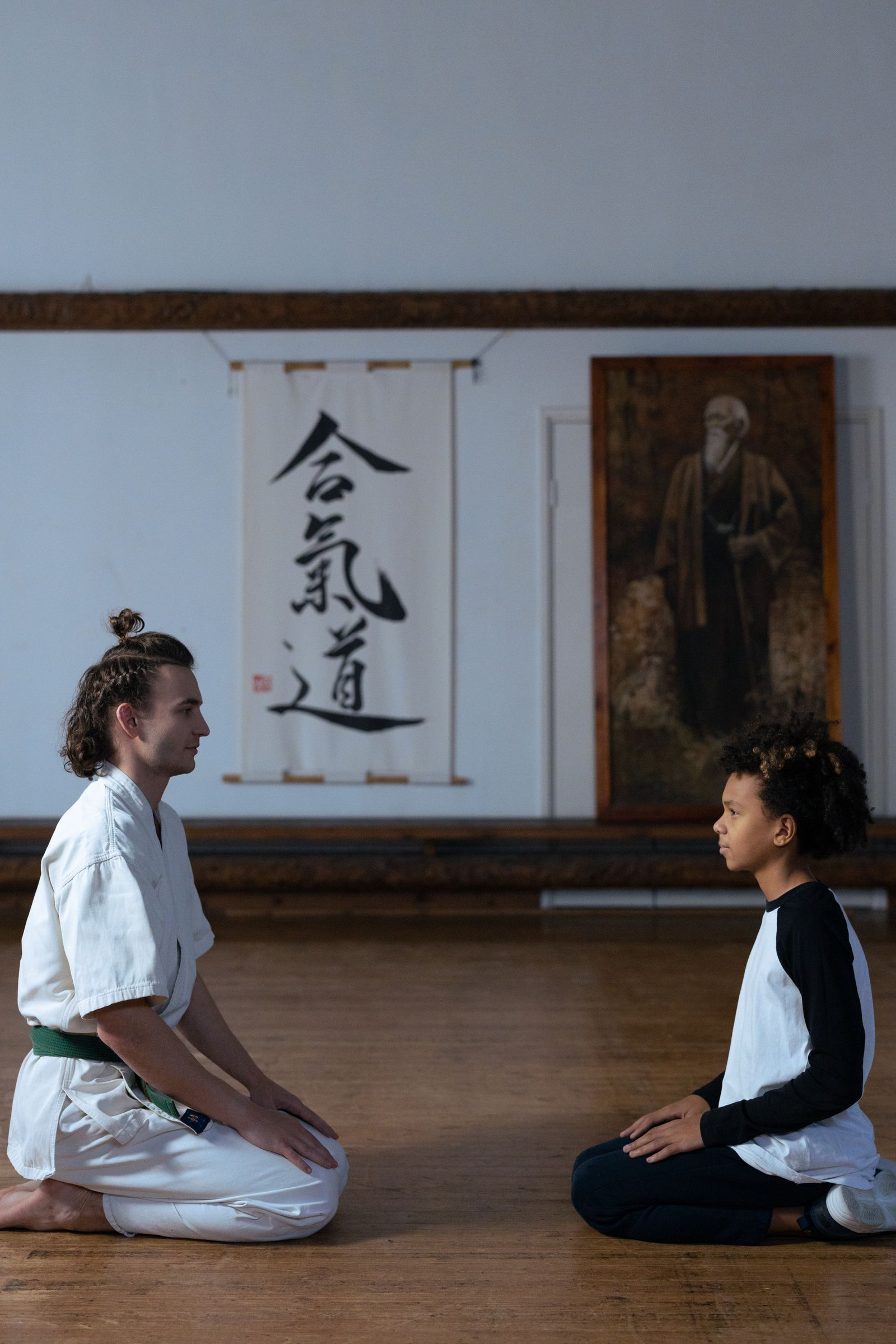 Pratiquant d’aïkido en seiza devant la calligraphie 合気道 et le portrait du fondateur