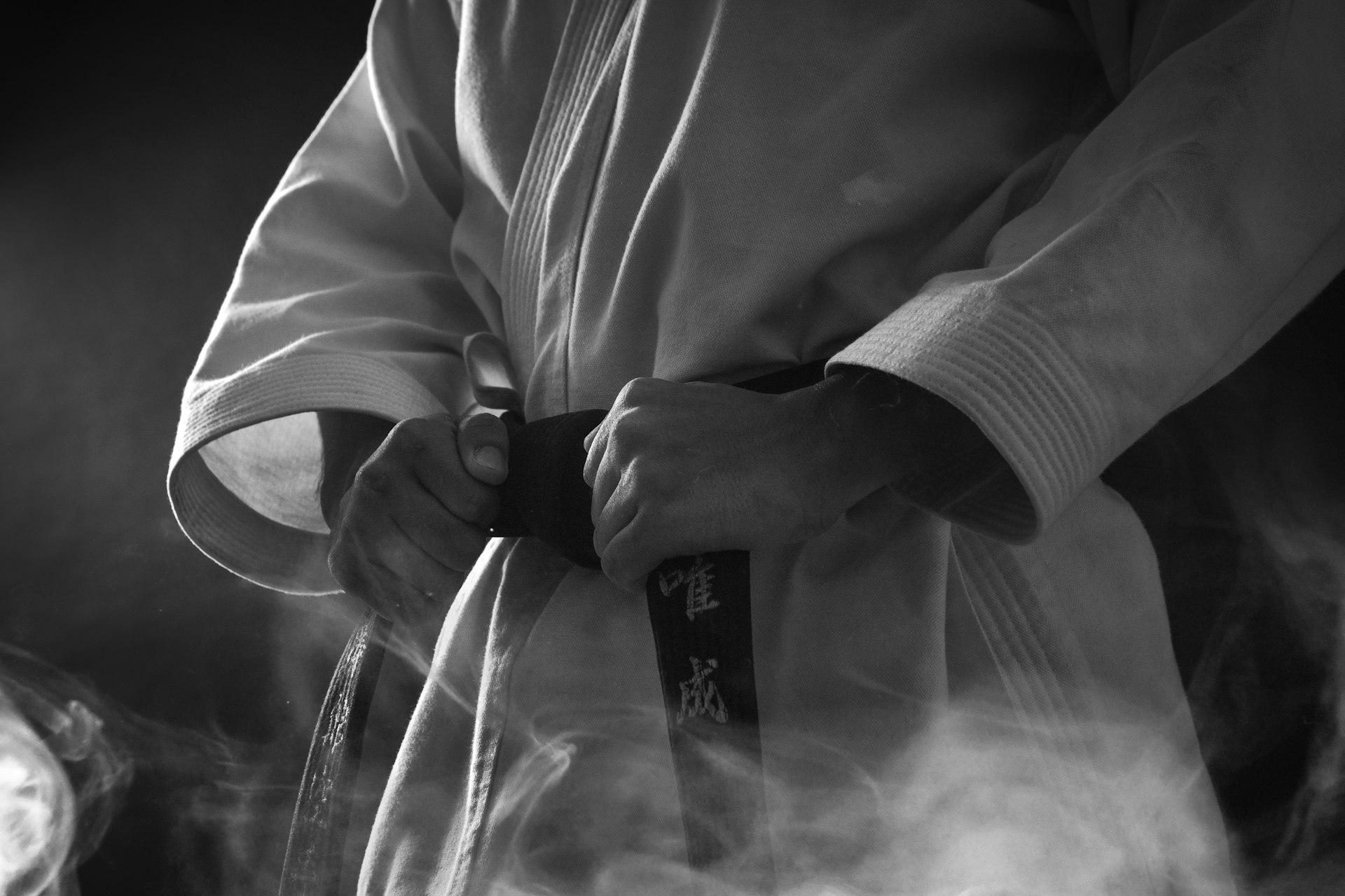 Gros plan en noir et blanc de mains nouant une ceinture noire de karaté